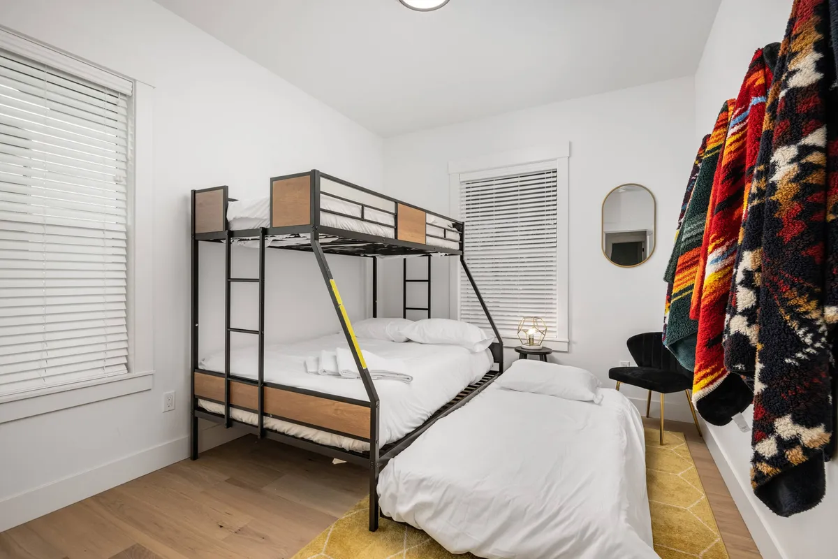 A comfortable and playful bedroom featuring a bunk bed with textured blankets, an accent chair, and a round mirror. The layered bedding and intimate layout create a cozy space for late-night chats or relaxing after a busy day.