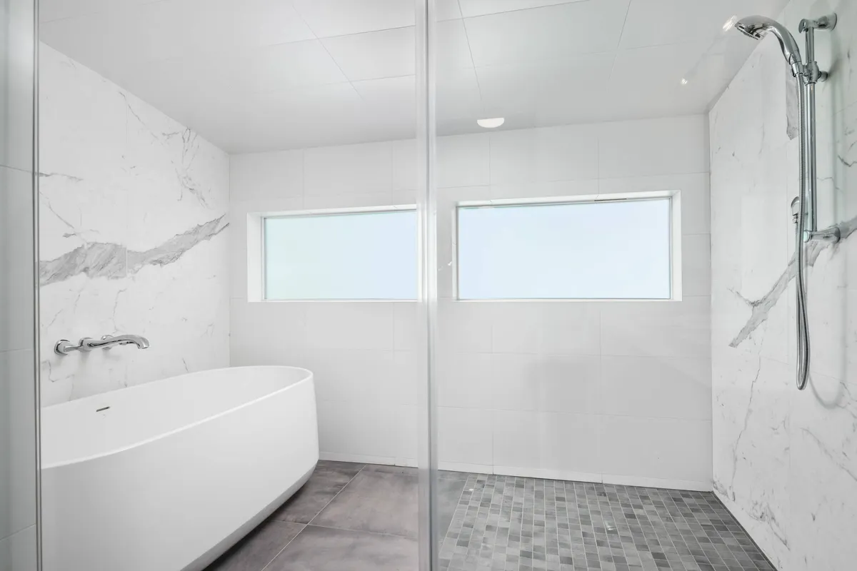 An elegant en suite bathroom featuring a freestanding soaking bathtub, a glass shower enclosure, and a marble accent wall. The space is designed for relaxation with a luxurious, spa-like feel.