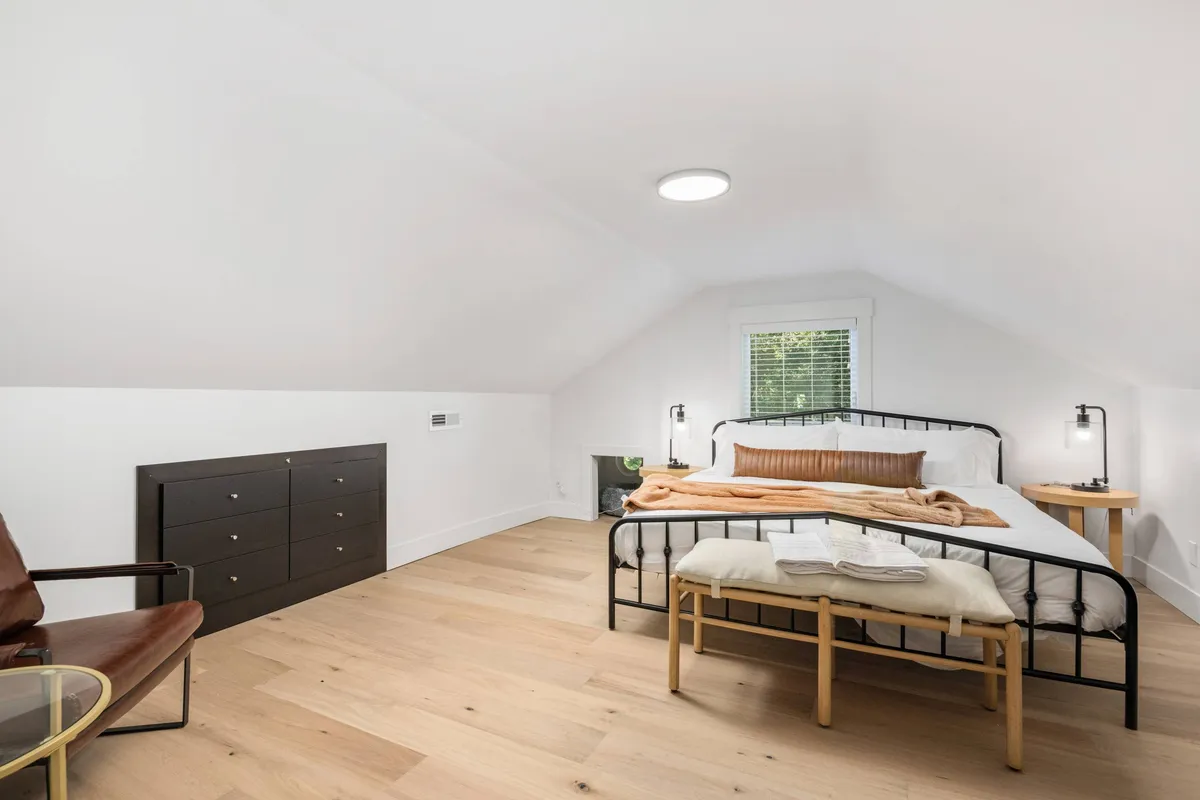A serene basement king bedroom featuring a large bed with cozy blankets, a wooden dresser, and a chair with a glass table by the window. The room feels private and inviting, offering a restful retreat after a night of fun.