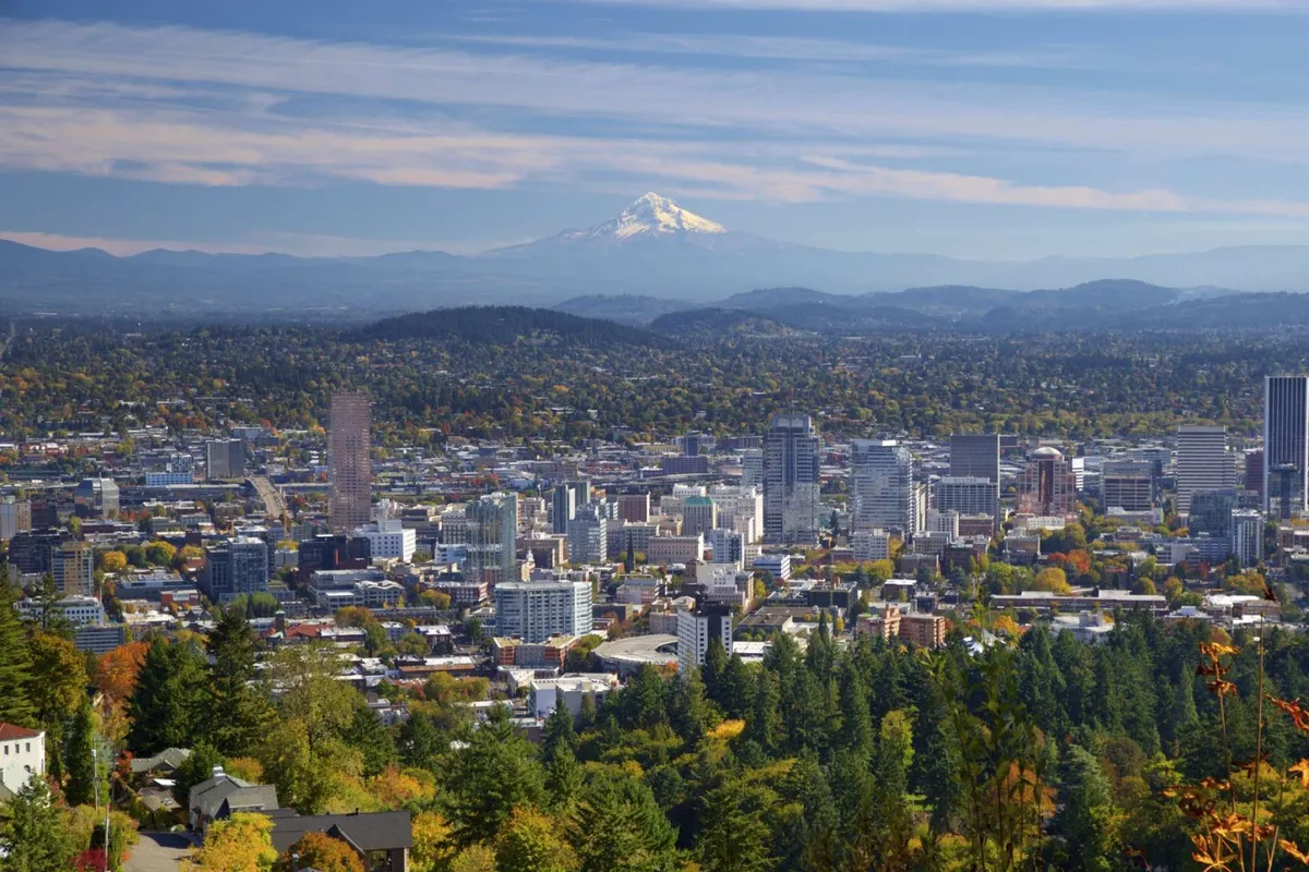 A panoramic view captures Mount Hood rising in the distance over Portland’s skyline, with lush forest in the foreground and the urban landscape stretching toward the horizon. The image is vibrant and inspiring, perfectly hinting at both the natural and urban attractions easily accessible from the property.