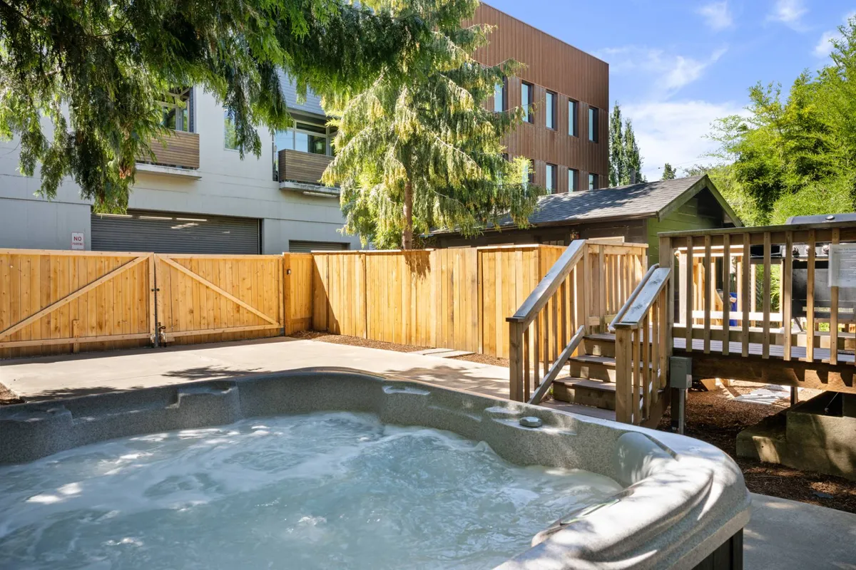 A tranquil backyard scene showcasing a hot tub set next to a wooden fence, surrounded by mature trees and greenery. The ambiance is peaceful, with hints of sunset light filtering through, promising relaxation and privacy.