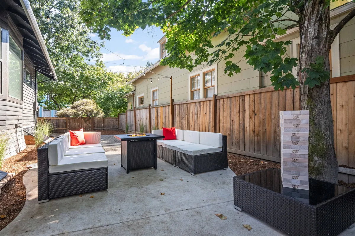 An inviting outdoor seating area with a fire pit, decorative pillows, and a wooden fence. The space is open, comfortable, and provides a secure environment suitable for pets and outdoor activities.