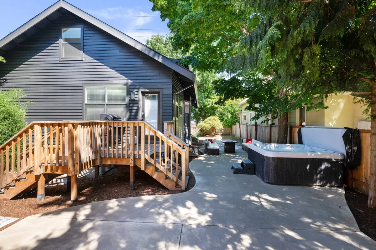 An inviting exterior view of a wooden ramp leading up to a deck with a steaming hot tub surrounded by lush greenery. The natural setting suggests relaxation and offers a tranquil spot to unwind after a day of adventure.