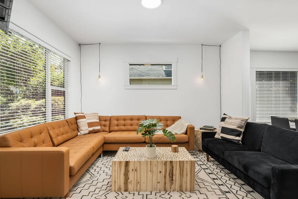 A spacious entertainment area with an orange sectional sofa, wooden coffee table, and black sofa, designed for both relaxation and social gatherings. Decorative touches like plants create a homey, lived-in feel, and the layout is perfect for both watching TV and socializing.
