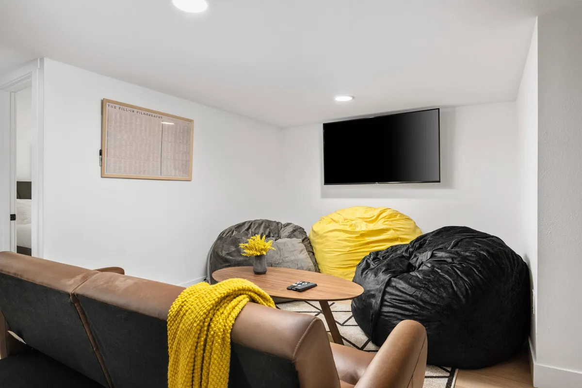 A cozy basement movie area with bean bag chairs circling a coffee table, all facing a large TV. The inviting setup encourages movie nights, relaxing, and casual socializing in an informal, family-friendly space.