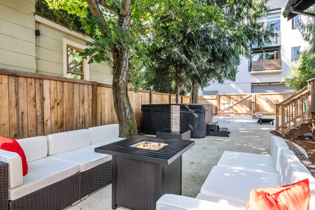 An inviting outdoor seating area featuring a cozy fire pit encircled by comfortable chairs, surrounded by lush trees and enclosed with a wooden fence. The setting is warm and private, ideal for gatherings or quiet moments outside.
